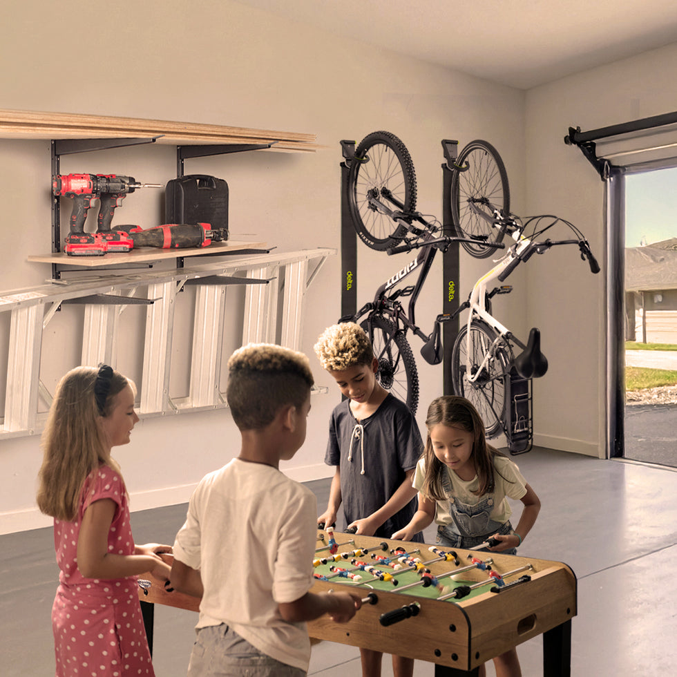 Children playing foosball in a garage with tools and bicycles on shelves.